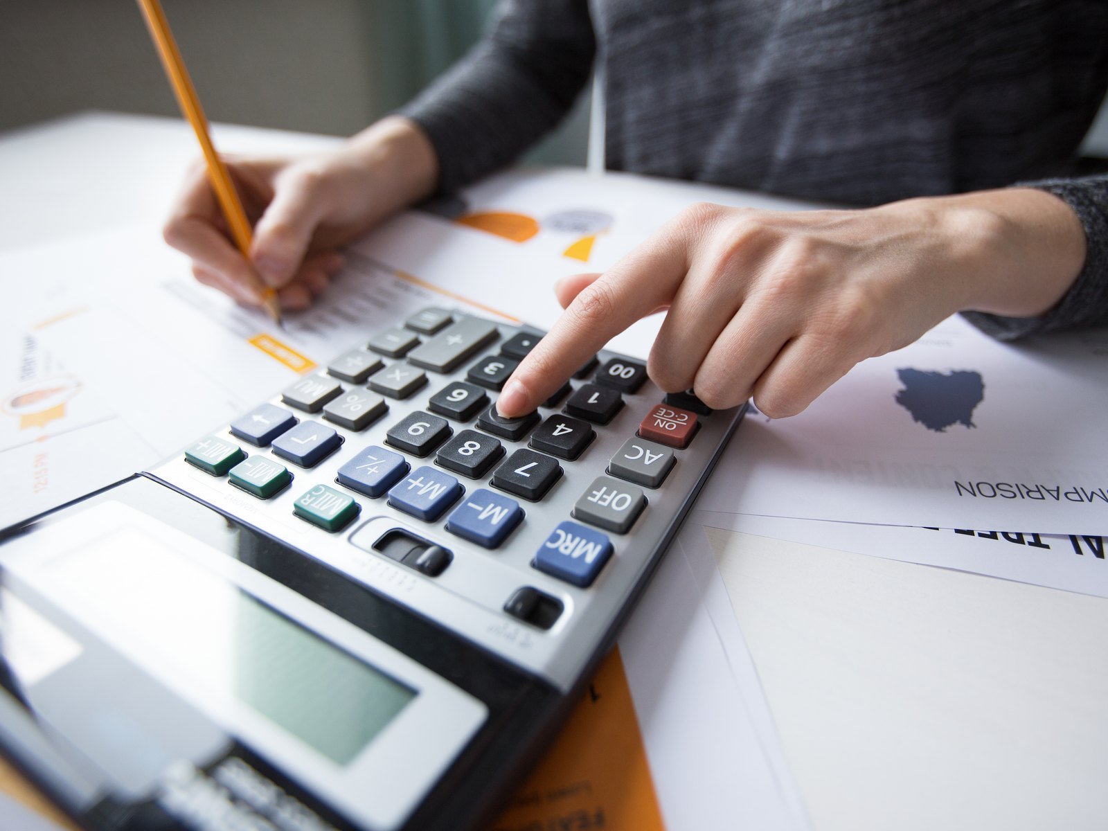 Manos de contadora usando una calculadora sobre reportes financieros